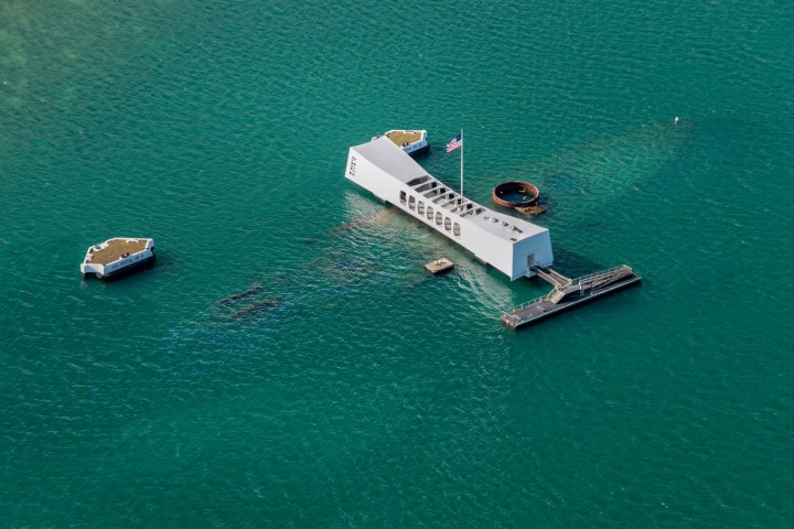 a small boat in a body of water with USS Arizona Memorial in the background