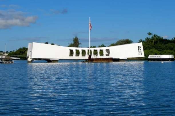 a small boat in a large body of water with USS Arizona Memorial in the background